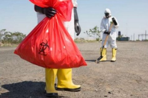 Workers in PPE and yellow boots hold red toxic waste bag