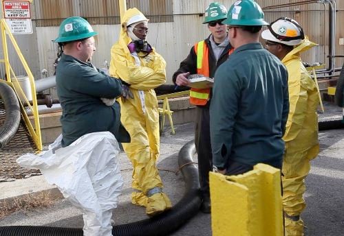 EHS experts in PPE suits and helmets discuss workplace safety