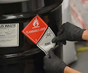 Worker places label on black 55-gallon drum