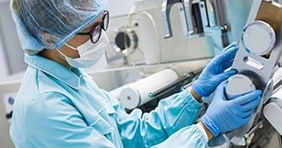 An employee wearing a mask, lab coat, and gloves works to complete an industrial hygiene program 