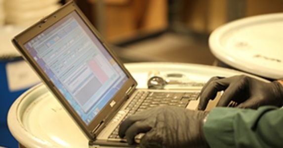 A scientist wearing gloves uses a laptop with chemical inventory software