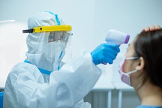 Worker in PPE suit temperature screens employee's forehead