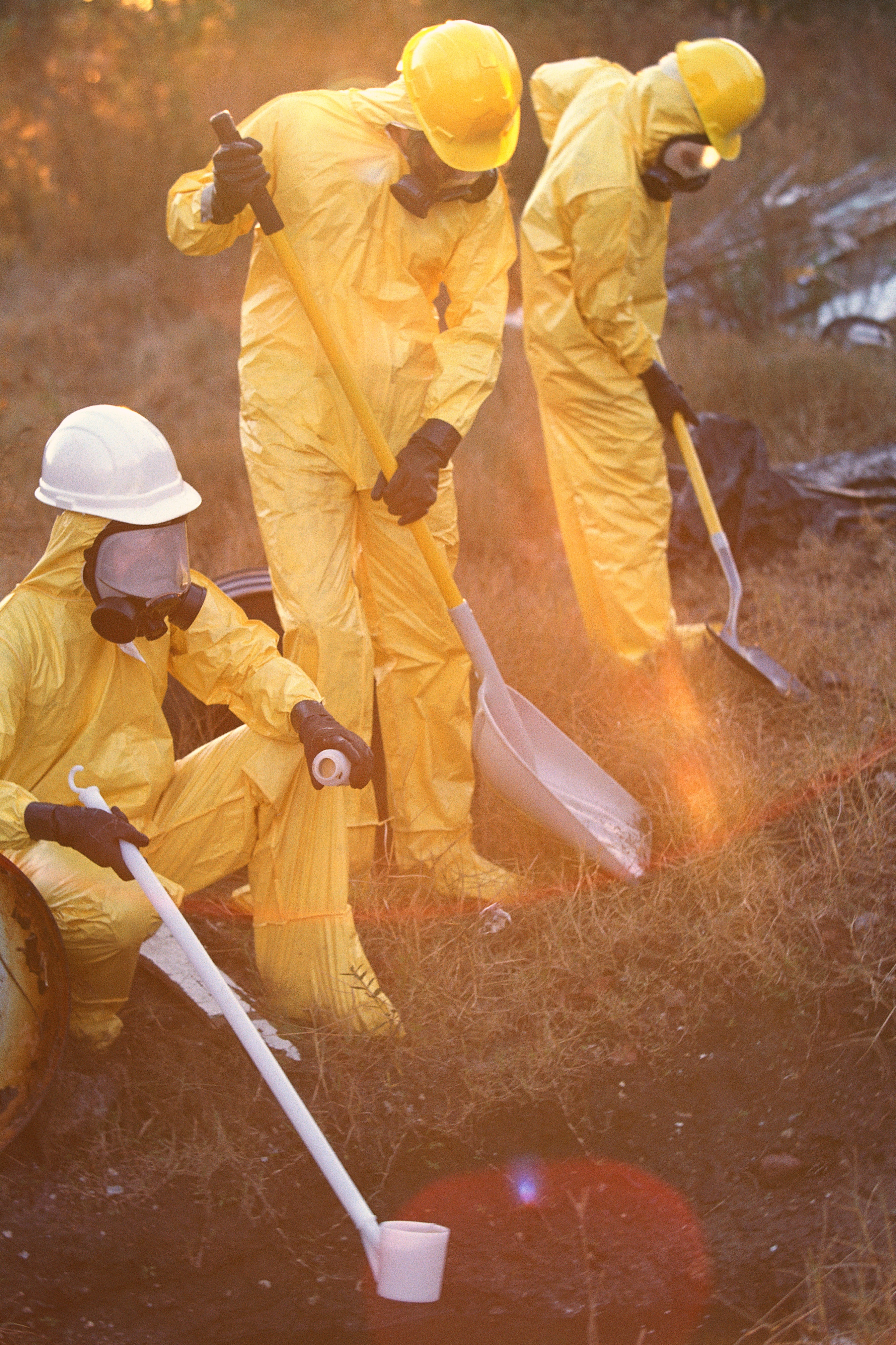 Workers in respirators, yellow PPE suits, and helmets work outdoors